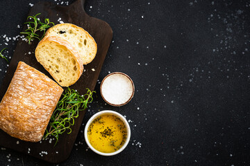 Sticker - Ciabatta bread on wooden board with olive oil, sea salt and herbs on black. Top view with copy space.