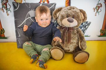 Wall Mural - Portrait of a cute and smiling baby boy sitting with his beloved teddy bear. Joy and happiness concept. Love and family emotion