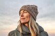 © Hanne Bauer - Medium shot portrait photography of a satisfied woman in her 40s that is wearing a warm beanie or knit hat against a sky and clouds background . Generative AI
