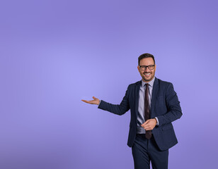 Portrait of smiling handsome marketing manager showing copy space for business advertisement. Happy male entrepreneur presenting and recommending new product while standing isolated on blue background
