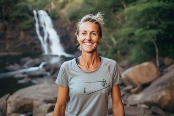 Wall Mural - Medium shot portrait photography of a grinning woman in her 40s that is wearing a casual t-shirt against a scenic hiking trail with a waterfall in the distance background . Generative AI