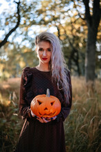 Beautiful young woman in brown dress holding carved pumpkin