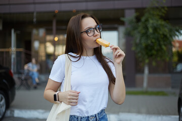 Wall Mural - Beautiful young woman eating in ice cream outdoor. Portrait of a pretty female person wearing cotton shopper bag and glasses