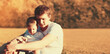 © guas - Portrait of happy young father and son child together sitting on grass in sunny evening park