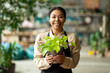 Portrait of happy black female botanist holding fresh plant in pot in gardening center. Successful botanist and store owner concept