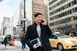 Young busy happy Asian business man office professional holding cellphone in hands walking on big city urban street making corporate business call, talking on cellular phone standing in downtown.