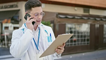 Poster - Young hispanic man doctor talking on smartphone reading document at coffee shop terrace