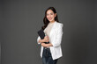 © Nutchapong Wuttisak - Asian female executive with long hair standing hugging a tablet for work, holding a pen, with a beautiful smile. wearing a white suit and stand to take pictures with a gray scene in the studio