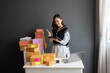 © Nutchapong Wuttisak - Asian female online shopping business owner Checking product orders through a tablet and happy smile Around there are customer order boxes waiting to be delivered to the post office in the office.