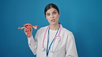 Wall Mural - Young beautiful hispanic woman gynecologist holding anatomical model of uterus speaking over isolated blue background