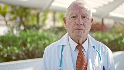 Wall Mural - Senior grey-haired man doctor standing with serious expression at park