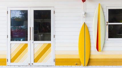 Colorful facade wall with surfboards hanging on it with door and window background.