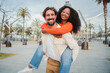 Multiracial couple embracing and having fun. Caucasian man giving his african american girlfriend a romantic piggyback ride enjoying a nice day together. Smiling guy in love carrying on back his woman