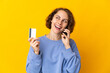 © luismolinero - Young English woman isolated on pink background keeping a conversation with the mobile phone and holding a credit card