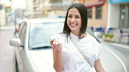 Wall Mural - Young beautiful hispanic woman holding key standing by car at street