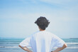 © HML - 夏の海岸に向かって立つTシャツ姿の男性