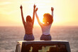 © Matthew Cerff/peopleimages.com - Sunset, women sitting on a car and at the beach with back view for carefree or peace. Freedom or adventure, summer vacation or holiday break and travel with female people at sea happy together