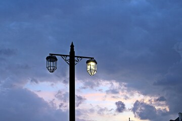 orange sunset on a partly cloudy evening and a lit lamp post with two lights