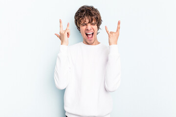 Wall Mural - Young caucasian man isolated on blue background showing a horns gesture as a revolution concept.