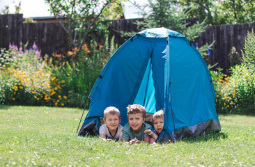 three little boys lie in a blue tourist tent in the yard. the concept of sports, summer holidays, hi