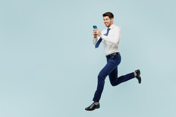 Full body young employee IT business man corporate lawyer in classic formal shirt tie work in office hold in hand use mobile cell phone isolated on plain pastel light blue background studio portrait