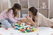 © fizkes - Joyful mom and cute little kid building toy city from colorful blocks, cubes, resting on heating floor, enjoying family playtime, leisure, learning game activity, smiling, laughing