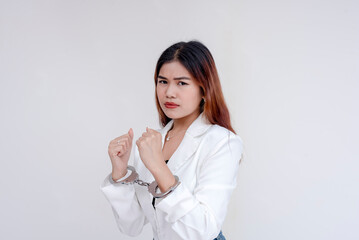 A sad and serious young woman holding her handcuffed hands up towards herself while looking at the camera. Isolated on a white background.