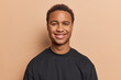 © wayhome.studio  - Cheerful young man with dark skin dressed casually in black tshirt smiles pleasantly looks directly at camera expresses genuine enjoyment isolated over brown background. People and emotions concept
