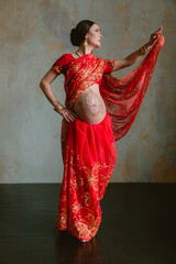 Pregnant woman in red sari. mehendi. Indian painting on woman's hands and pregnant belly with henna tattoo on room background