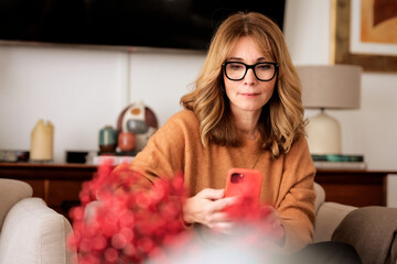 Poster - Close-up of blond haired woman relaxing in an armchair at home and using mobile phone