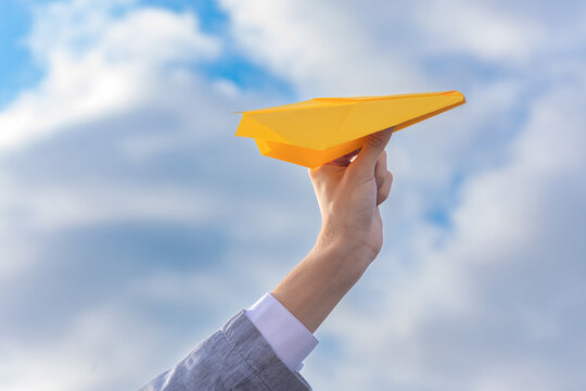 Wall Mural - flight, freedom concept, a hand holds a bright yellow paper plane against a blue sky
