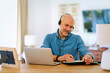 © gzorgz - Mid aged man with headset sitting at home and using laptop