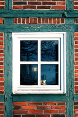 Window with a flower pot on the wall of an old half-timbered house in Germany. The branches of a tree, a fence and the light of a lantern are darkly reflected in the window glass.