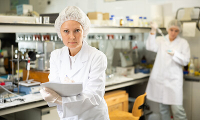 Middle-aged woman chemist writing report on results of chemical experiments in research center