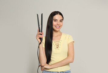 Poster - Beautiful happy woman with hair iron on light grey background