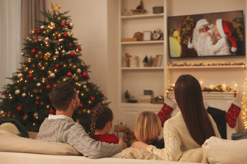 Wall Mural - Family watching Christmas movie via TV in cosy room, back view. Winter holidays atmosphere