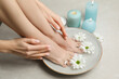 © New Africa - Woman soaking her feet in bowl with water and flowers on grey marble floor, closeup. Pedicure procedure