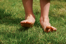 Happy Child Is Barefoot On The Grass, Close-up Feet, Enjoying Sunny Summer Day During Vacation. Tick Bite Prevention Concept, Use Of Repellents, Avoiding Tall Grass And Thickets.  World Soil Day
