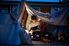 シーツで作ったテントの中で本を読んでいる兄弟