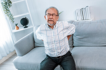 Wall Mural - An agonizing senior man in need of assistance while sitting on his sofa at home, suffering from back pain. Senior care, nursing home for pensioners, deteriorating health of old age.