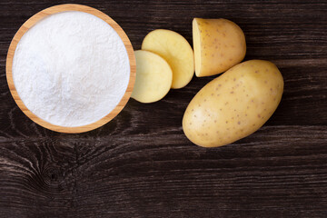 Wall Mural - Potato powder in wooden bowl and fresh potatoes with slice isolated on wooden table background. Top view. Flat lay.