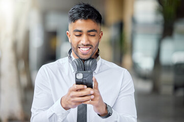 Business man, phone text and city of a professional with headphones watching a video. Urban, smile and Indian male person with work travel, mobile streaming and happiness with cellphone app and web