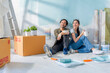 Asian Cheerful young marry couple having coffee break sitting among paint tools and accessories during the break in new apartment,home relocation renovate interior concept,happiness couple paint wall