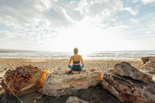 Woman Meditating Sitting On Rock At Beach