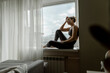 © Westend61 - Thoughtful woman relaxing on window sill at home