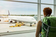 © Westend61 - Woman with backpack looking at plane through window at airport