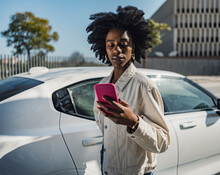 Young Woman Using Smart Phone Standing By White Car