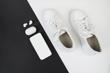 Top view photo of white sneakers with phone and headphones on black and white background