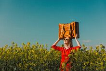 Smiling Woman Carrying Suitcase On Head In Rapeseed Field