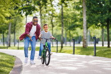 Happy Ethnic Family Father Teaches Child  Son  To Ride Bike In Park  .